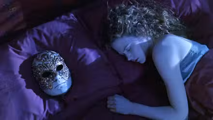 Alice (Nicole Kidman) está deitada na cama, aparentemente dormindo profundamente com uma máscara de porcelana branca e fria de um rosto masculino calmo deitado no travesseiro ao lado dela em De Olhos Bem Fechados.