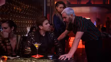 CHRIS MESSINA como Victor Zsasz se inclina em uma mesa para conversar com EWAN McGREGOR sentado como Roman Sionis, com JURNEE SMOLLETT-BELL como Canário Negro ao fundo, em “Aves de Rapina (E A FANTÁBULA EMANCIPAÇÃO DE UMA HARLEY QUINN) da Warner Bros.