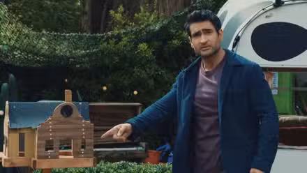 Kumail Nanjiani no Taskmaster UK apontando para uma casa de madeira.