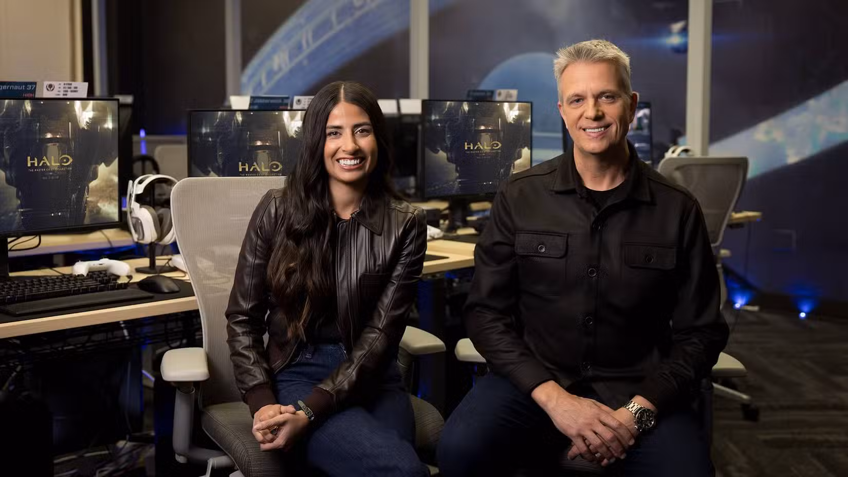 Asha Sharma sentou-se ao lado de Matt Booty em frente aos monitores que mostravam a coleção Halo Master Chief.