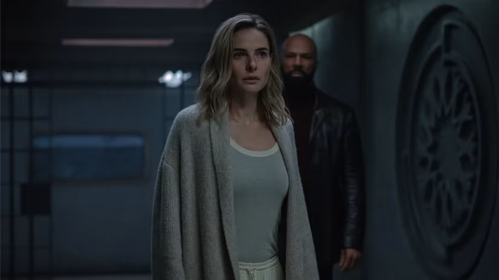 Juliette Nichols (Rebecca Ferguson) vestindo um suéter e pijama fica na frente de Robert Sims (Common) perto de uma cela de prisão aberta em Silo.
