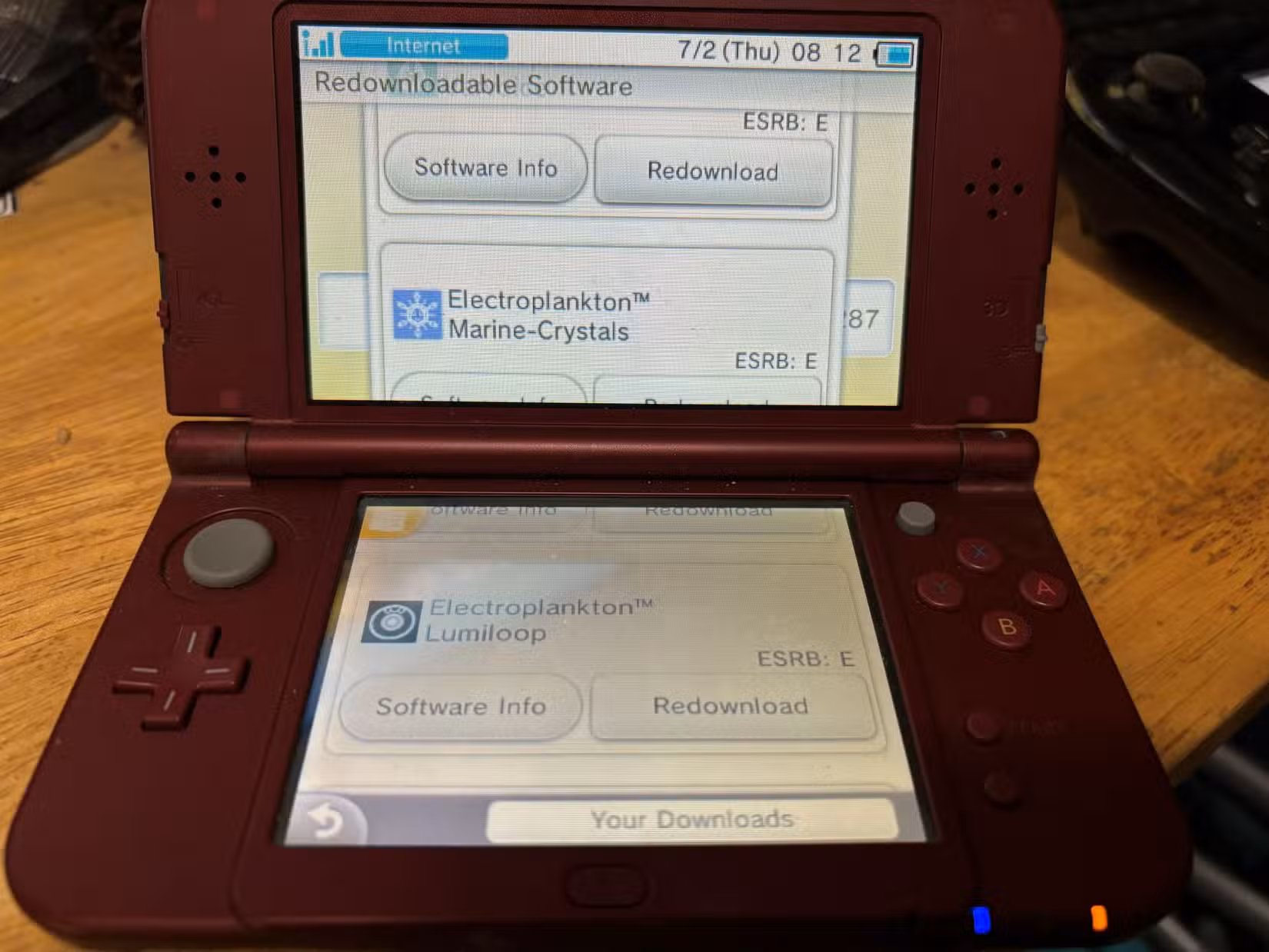 Um console Nintendo 3DS vermelho aberto com uma tela oferecendo um novo download do Electroplankton Lumiloop