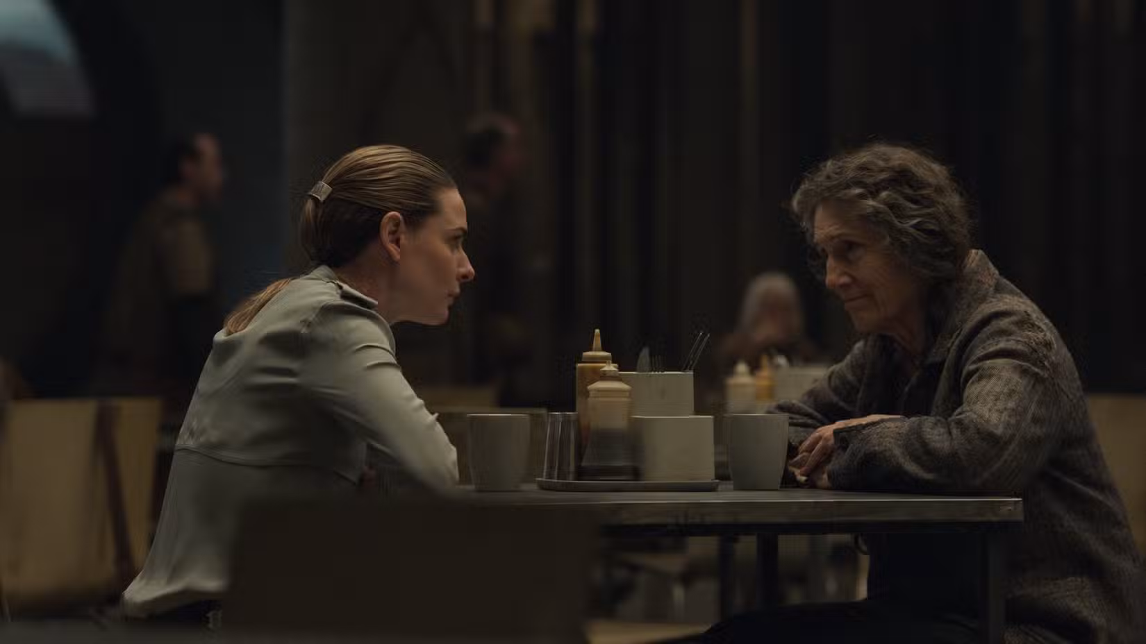Juliette Nichols (Rebecca Ferguson) senta no refeitório e conversa com Martha Walker (Harriet Walter) em Silo
