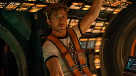 Ryan Gosling fazendo uma espécie de cara de pato interrogativa diante de um monitor de computador.