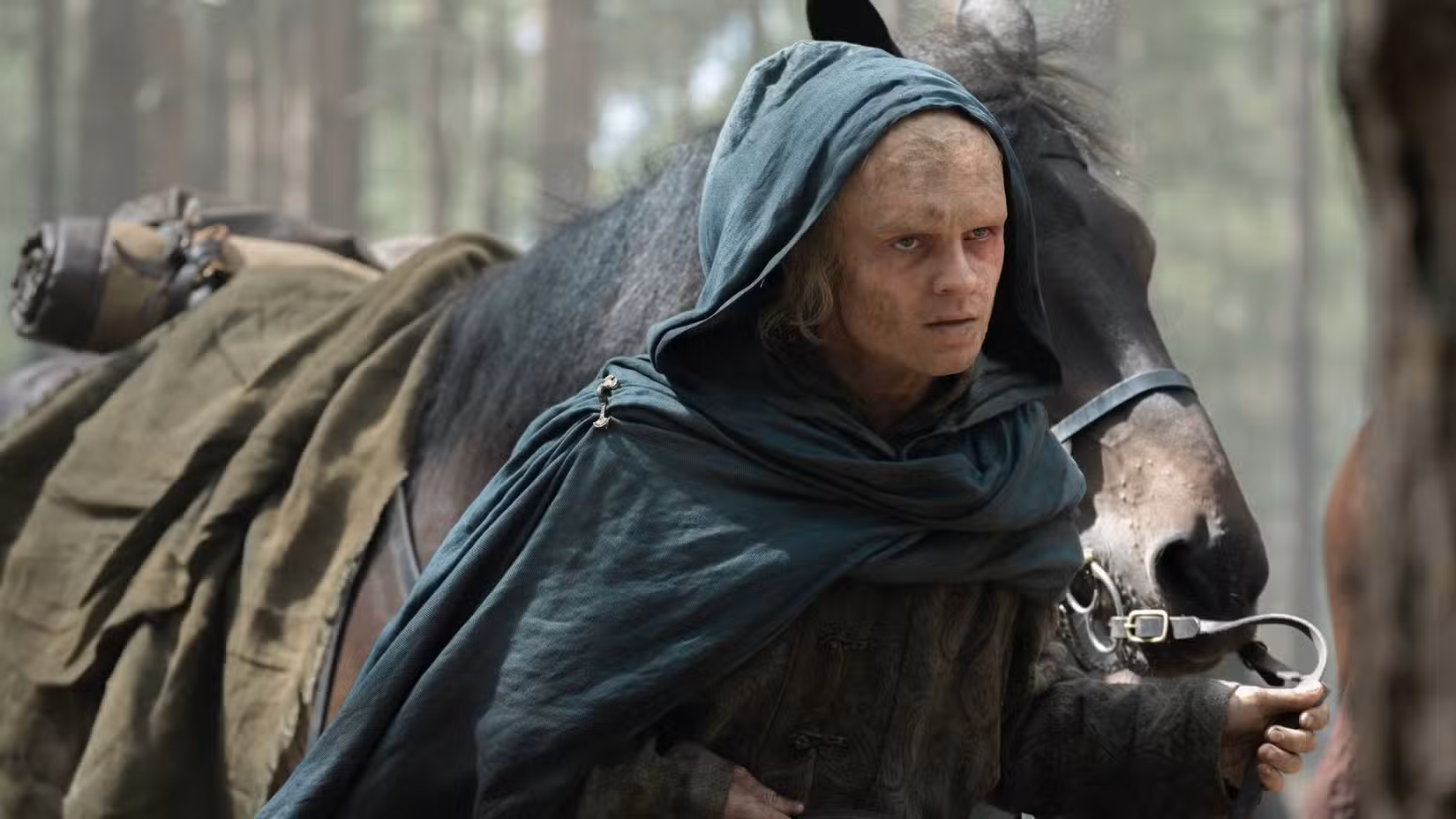 Rei Aemond (Tom Glynn-Carney) vestindo uma capa azul conduz um cavalo pelas rédeas na 3ª temporada de House of the Dragon.