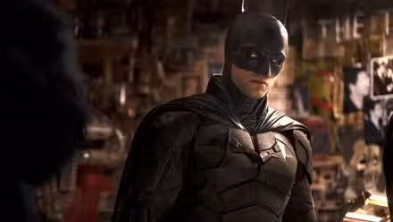Robert Pattinson como Batman em frente a uma parede de enigmas do Charada