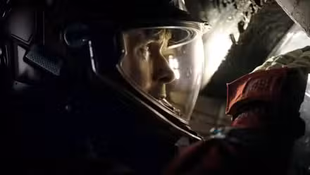 Em um espaço escuro e estreito, o astronauta Ryland Grace (Ryan Gosling), em traje espacial completo e capacete, espia através de uma pequena abertura no Projeto Ave Maria