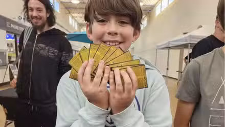 Um jovem de Alberta segura 10 cartas douradas de Mega Darkrai de um evento de pré-lançamento de Pitch Black.