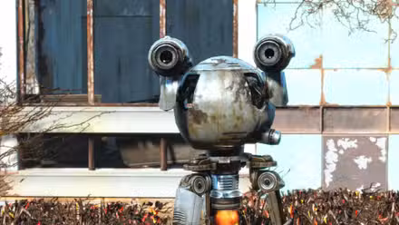 Um close de Codsworth, flutuando em frente a uma casa em ruínas no Santuário