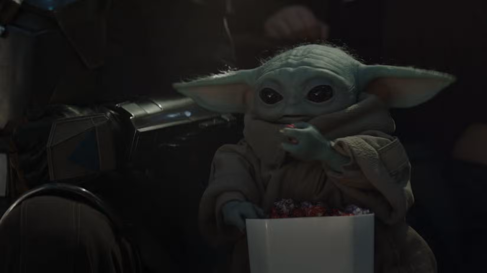 Grogu come pipoca enquanto está sentado ao lado de Din Djarin em uma partida de gladiadores em The Mandalorian e Grogu.