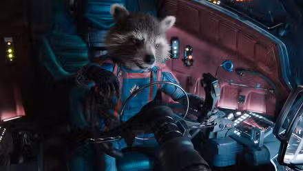O guaxinim antropomórfico Rocket (corpo interpretado por Sean Penn, dublado por Bradley Cooper) está sentado na cabine de uma nave espacial com uniforme completo de macacão azul e vermelho dos Guardiões da Galáxia em Guardiões da Galáxia Vol. 3