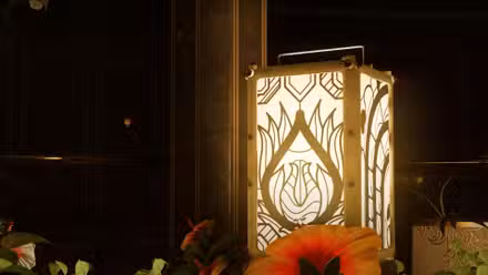 Um close de uma lanterna ornamentada com um padrão de flor, cercada por flores reais.